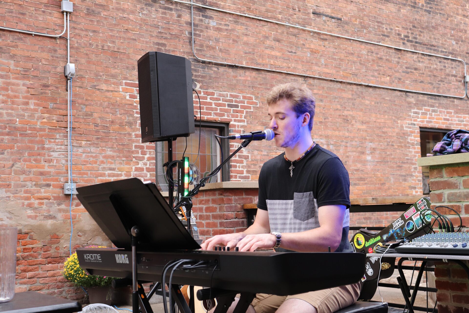 Ryan Howe playing keyboard and singing outdoors in front of a brick wall